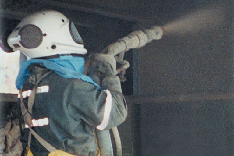 Worker spraying dry shotcrete in a supplied-air helmet system