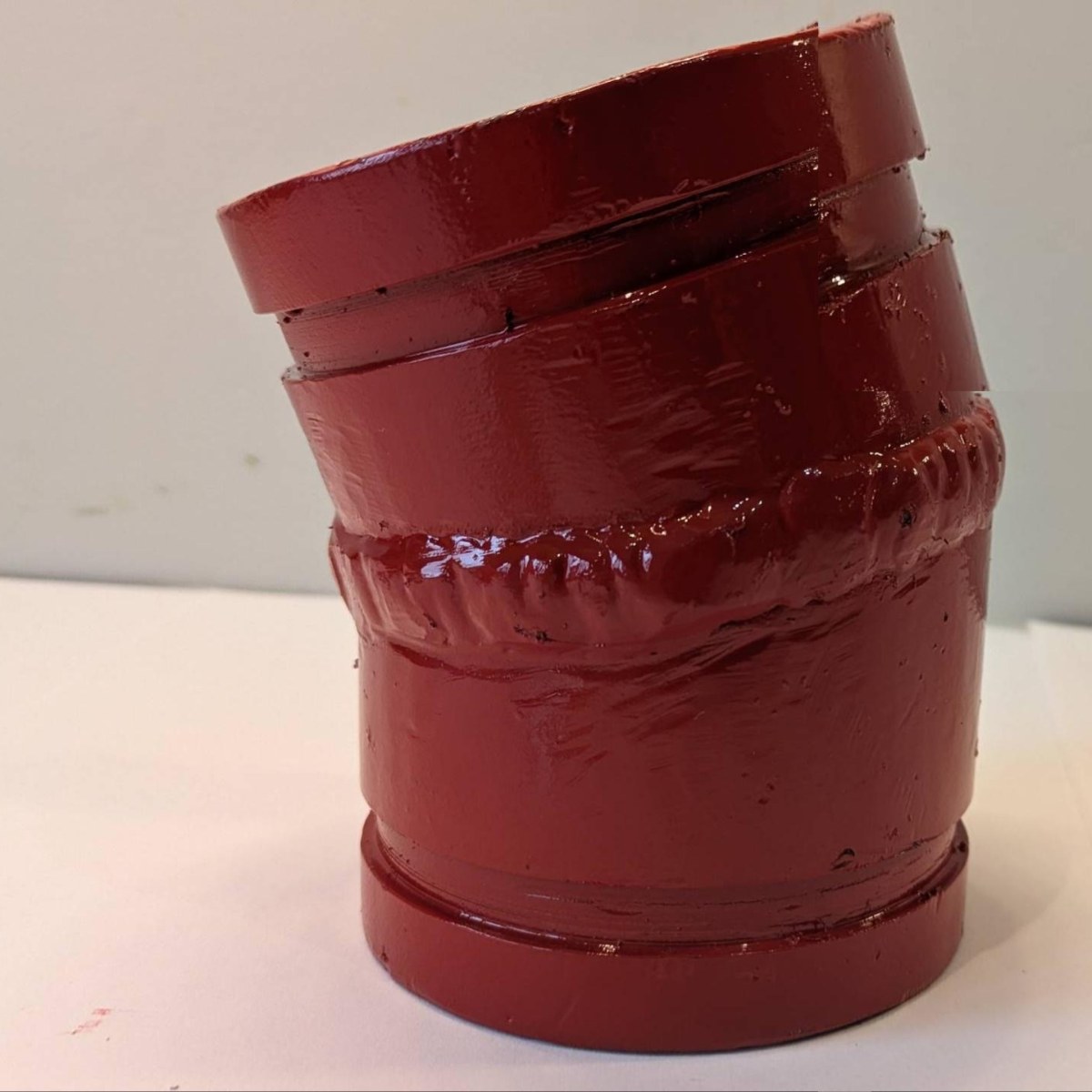 Fabricated 3" 22.5&deg; compact mitred Hrd67 elbow standing on a bench, red enamel, the girth weld at the mitre and the groove at each end
