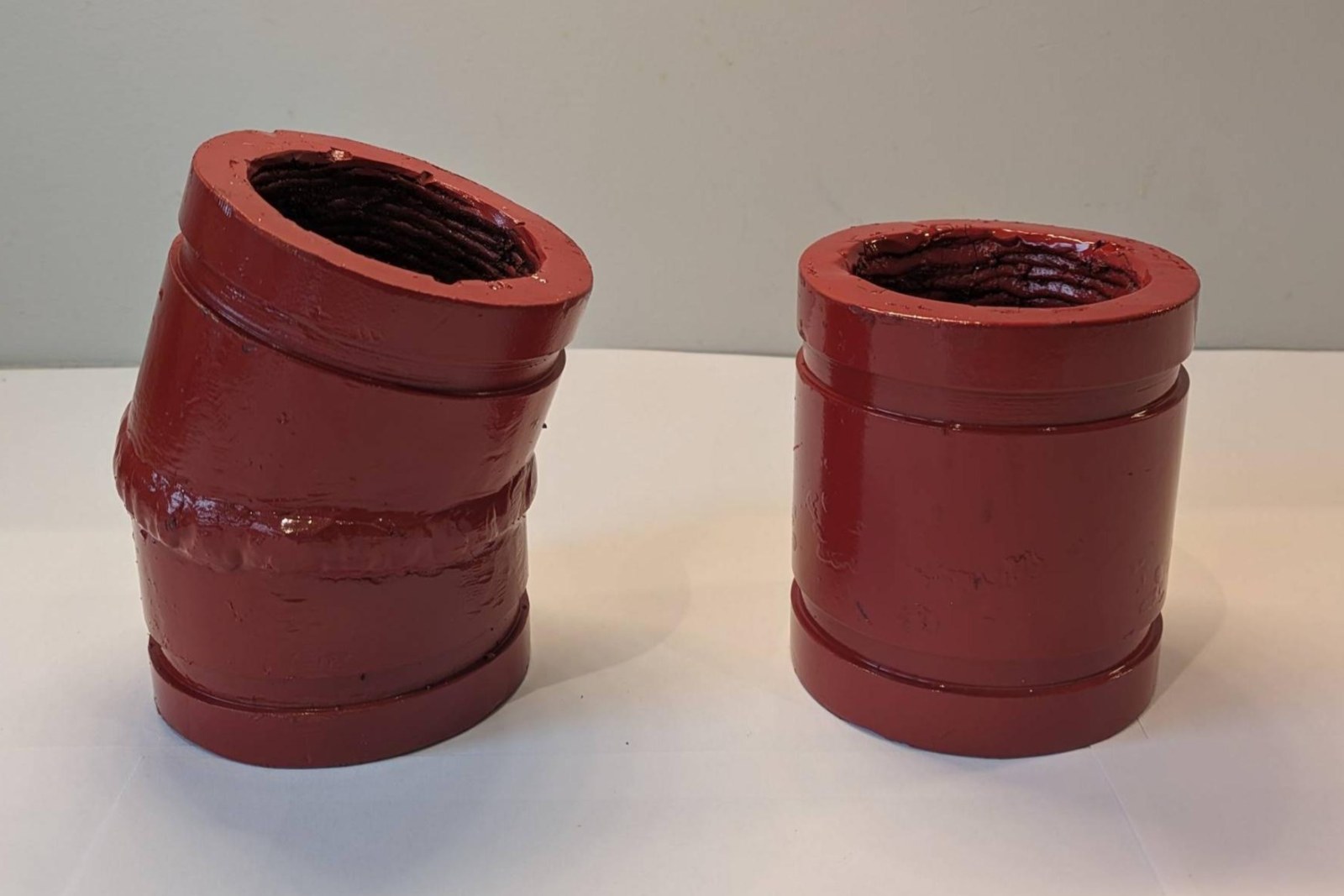Two fabricated Hrd67 components in red enamel on a bench &mdash; a 3" 22.5&deg; compact mitred elbow with the girth weld visible, and a 3" &times; 4" grooved spool, both with the bare weld deposit showing at the open ends