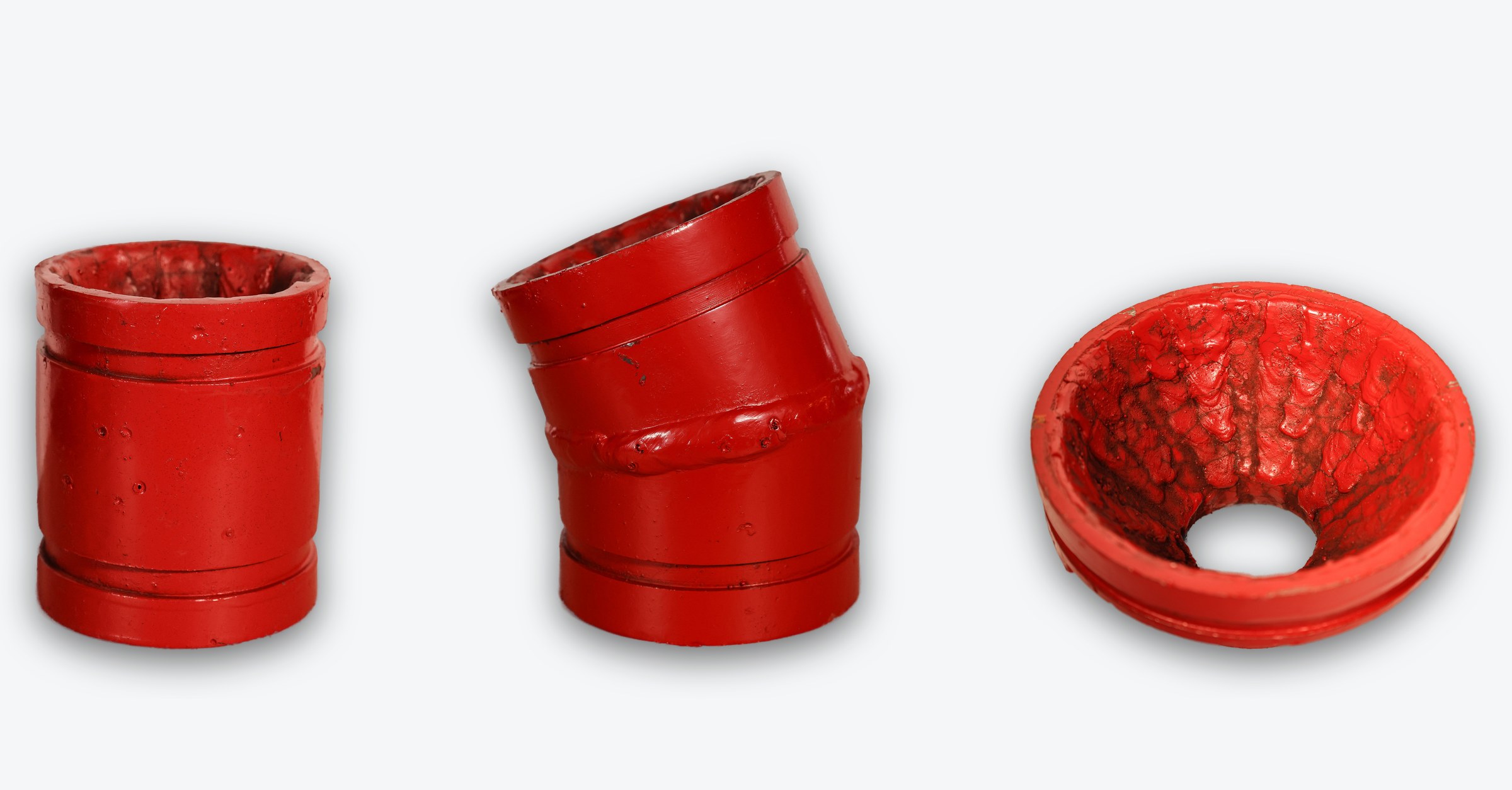 Three grooved fittings overlaid with Hrd67 and finished in red enamel &mdash; a 3" &times; 4" stub, a 3" 22.5&deg; elbow, and a 6&times;3 concentric reducer seen from above with the weld deposit visible across its bore