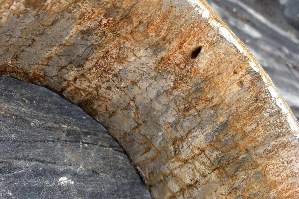 Close-up of the wall of a removed wear component: the surface crazed and scoured by the slurry, with the perforation where the wall finally wore through